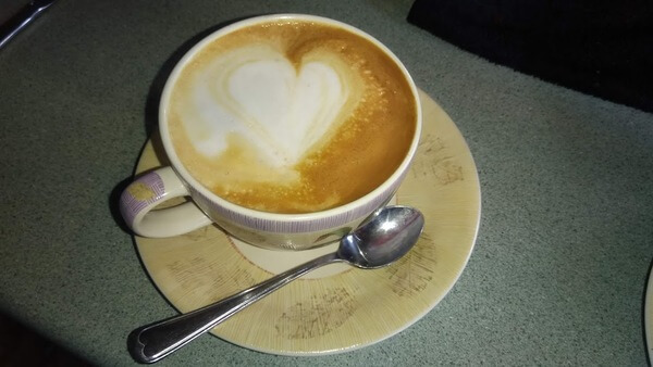 A flat white coffee on a plate with a teaspoon.